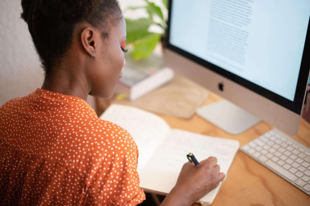 An image of a woman sitting at a desk, at work, writing on her notepad.
